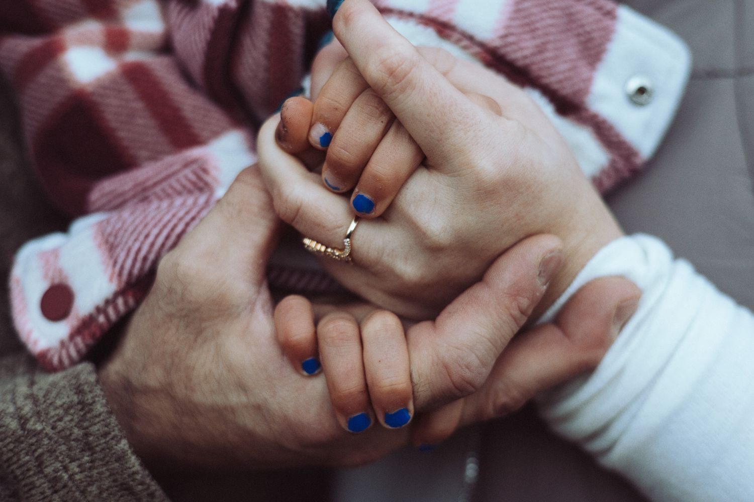 Hands with blue nail polish shown against a plaid shirt background.