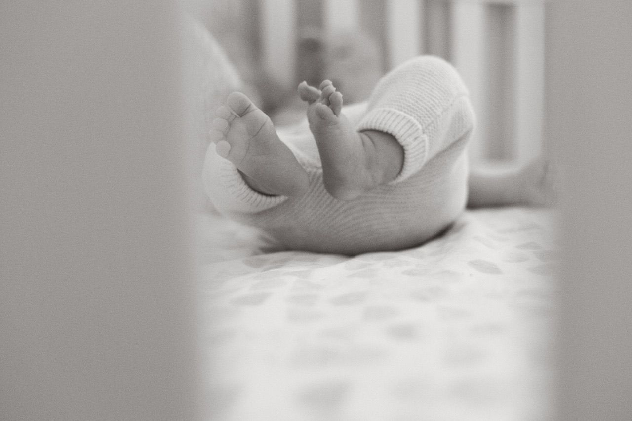 Black and white series of a baby resting peacefully on white bedding.
