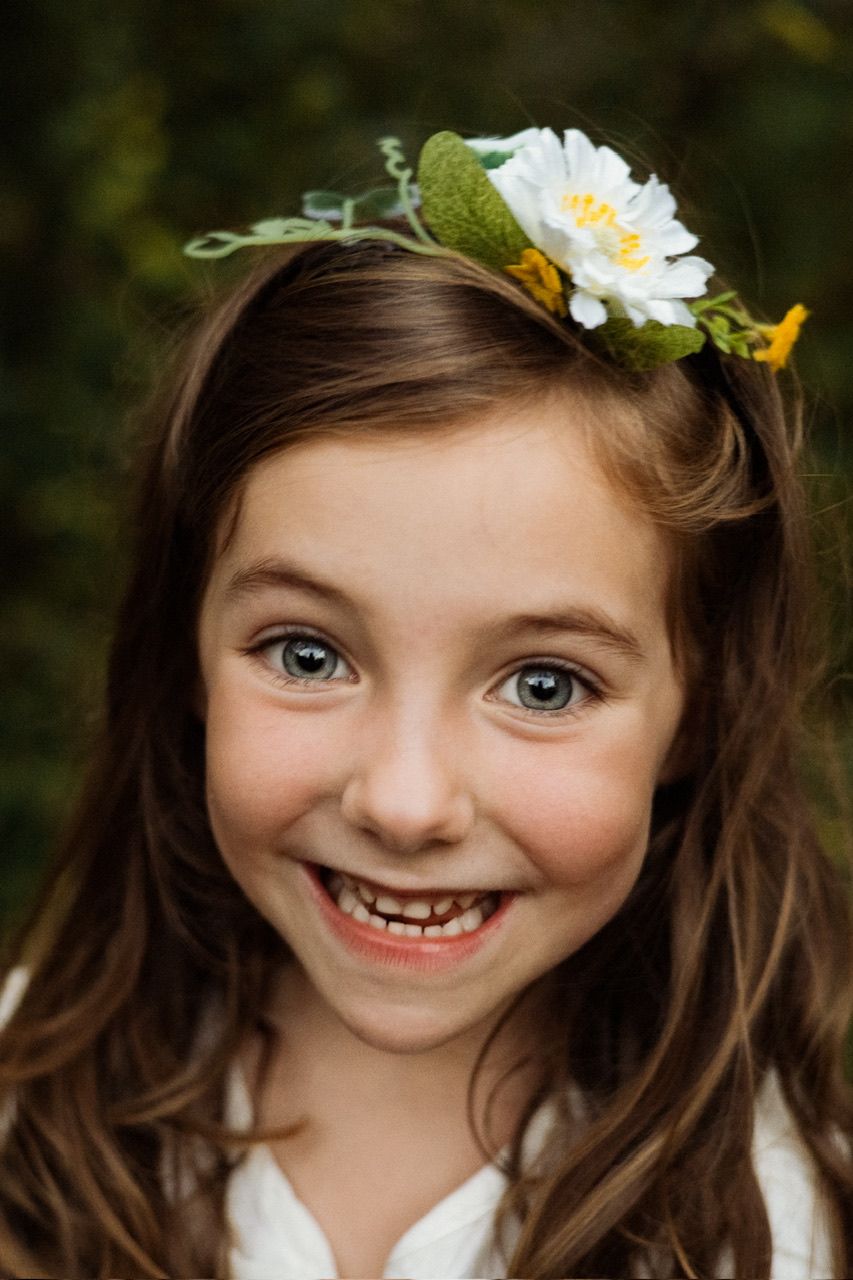 Close up portrait with white flowers in hair showing playful expressions and bright eyes.