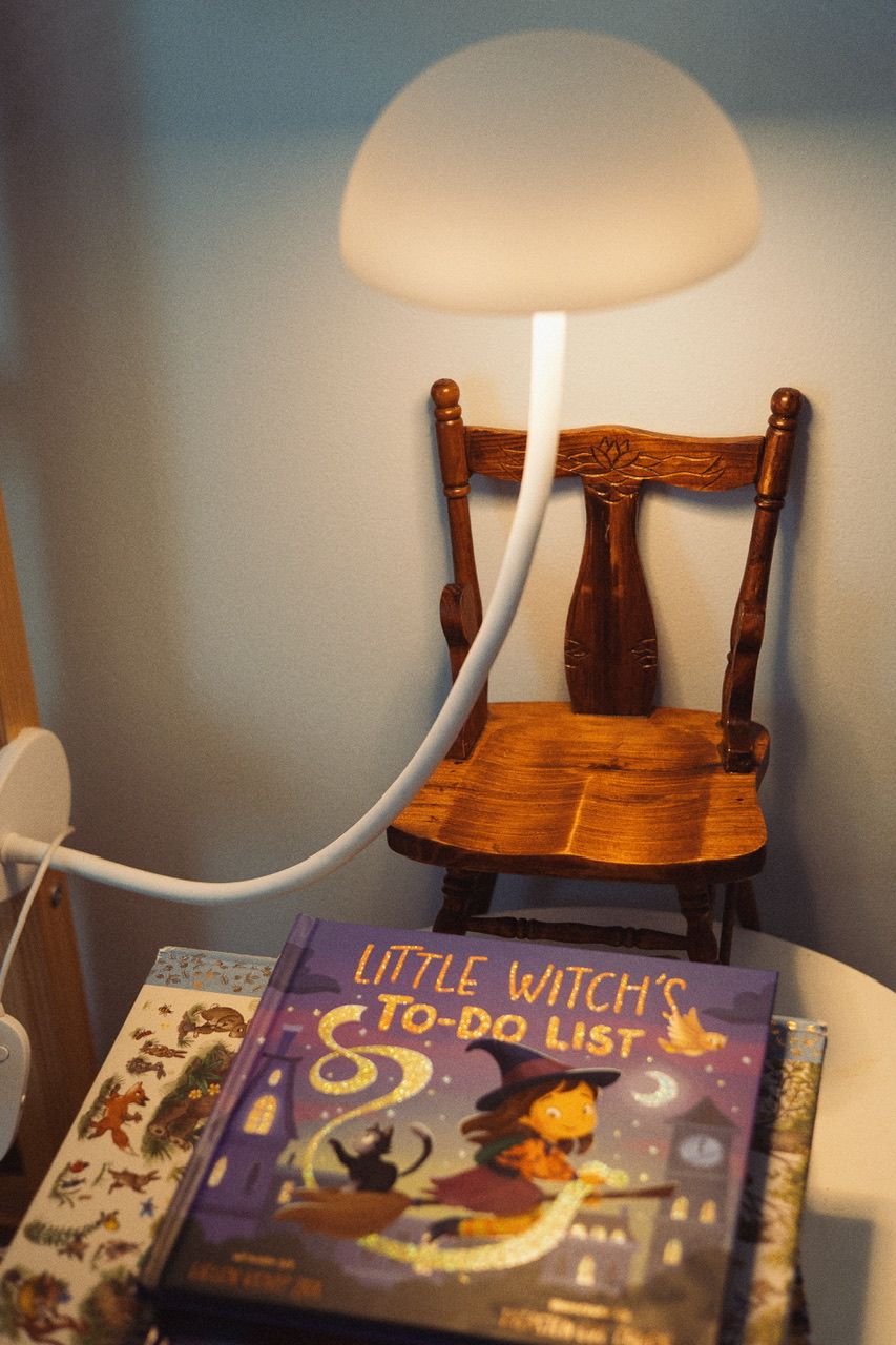Children's books including 'Little Witch's To-Do List' displayed on wooden chair under warm lighting.