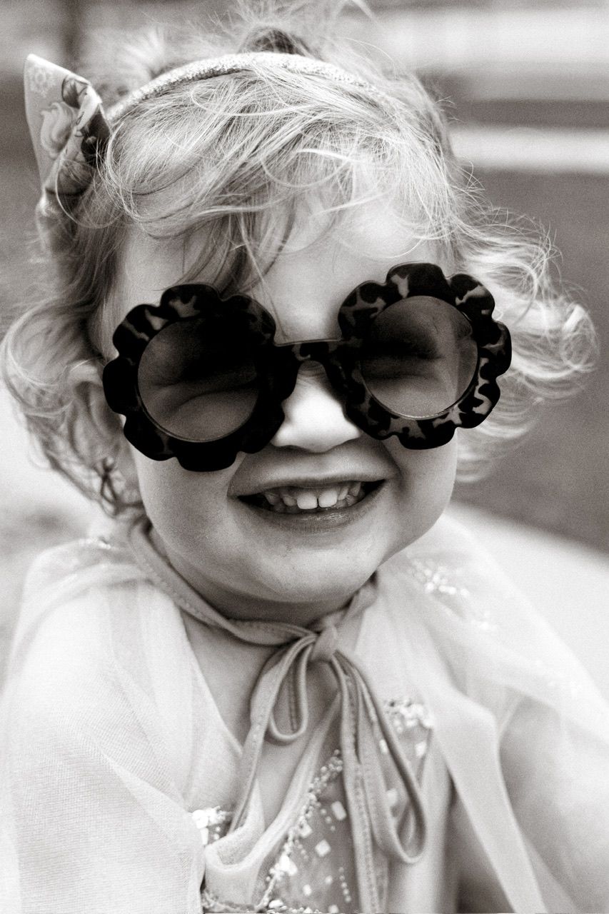 Black and white photo of a child wearing decorative floral sunglasses and smiling brightly.