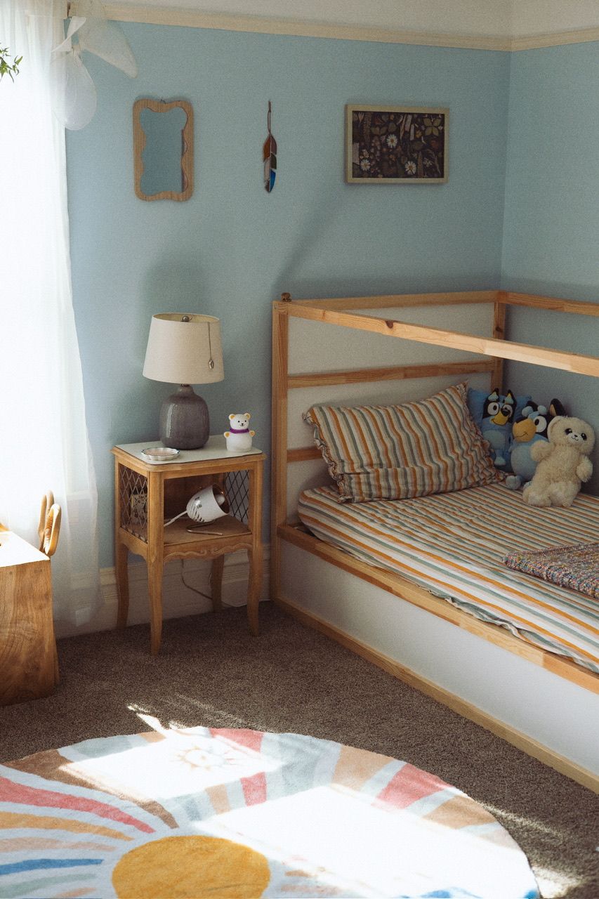 Children's bedroom with wooden bed frames and blue walls lit by natural sunlight.