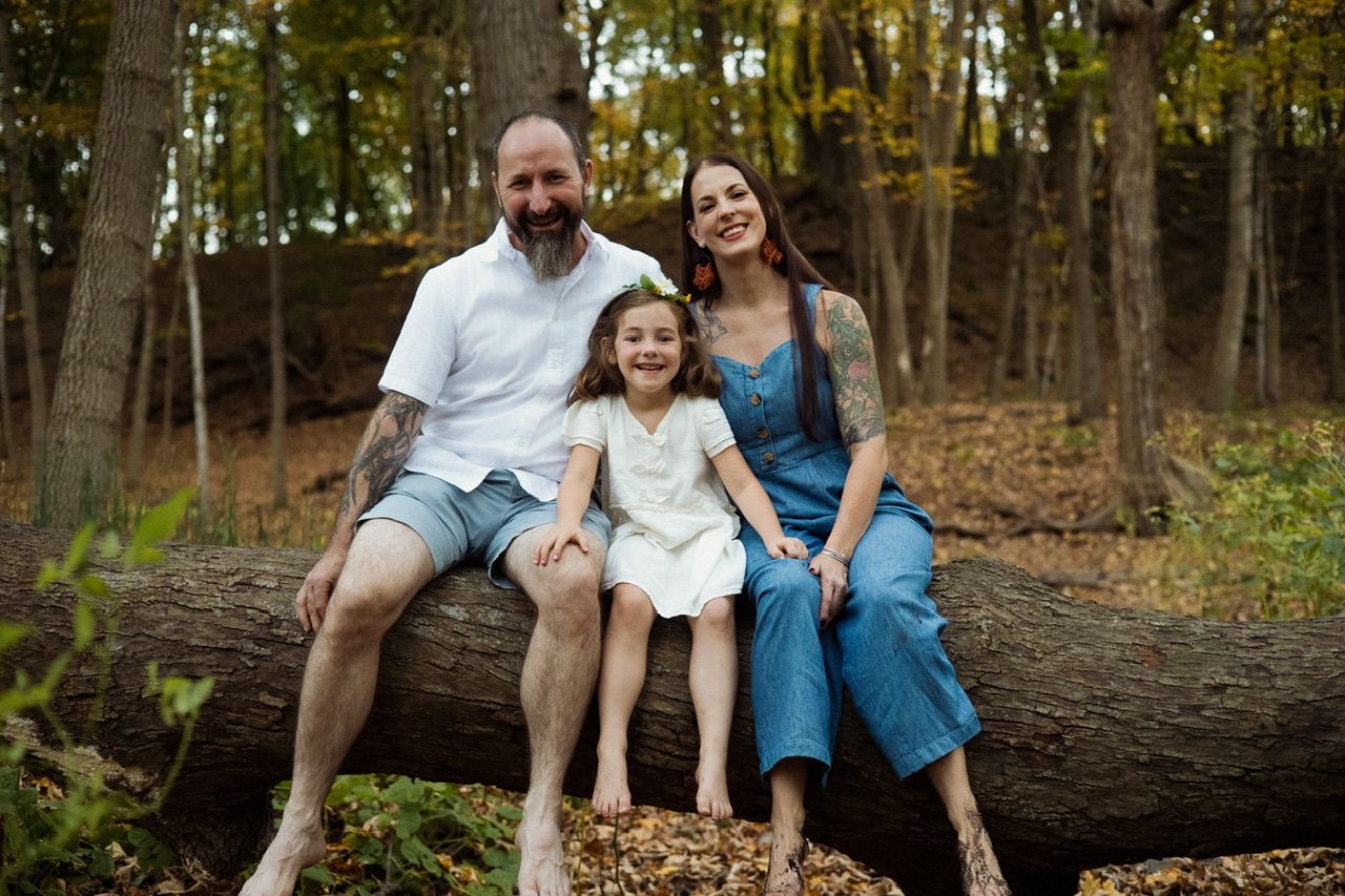 A family sits together on a fallen log in an autumn forest setting.