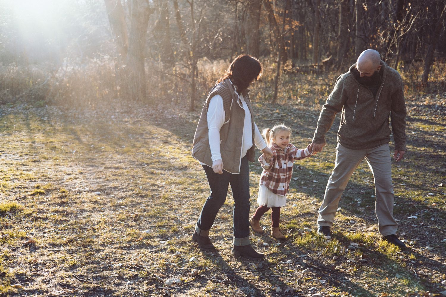 Family silhouettes walking together in a sunlit autumn field at golden hour.