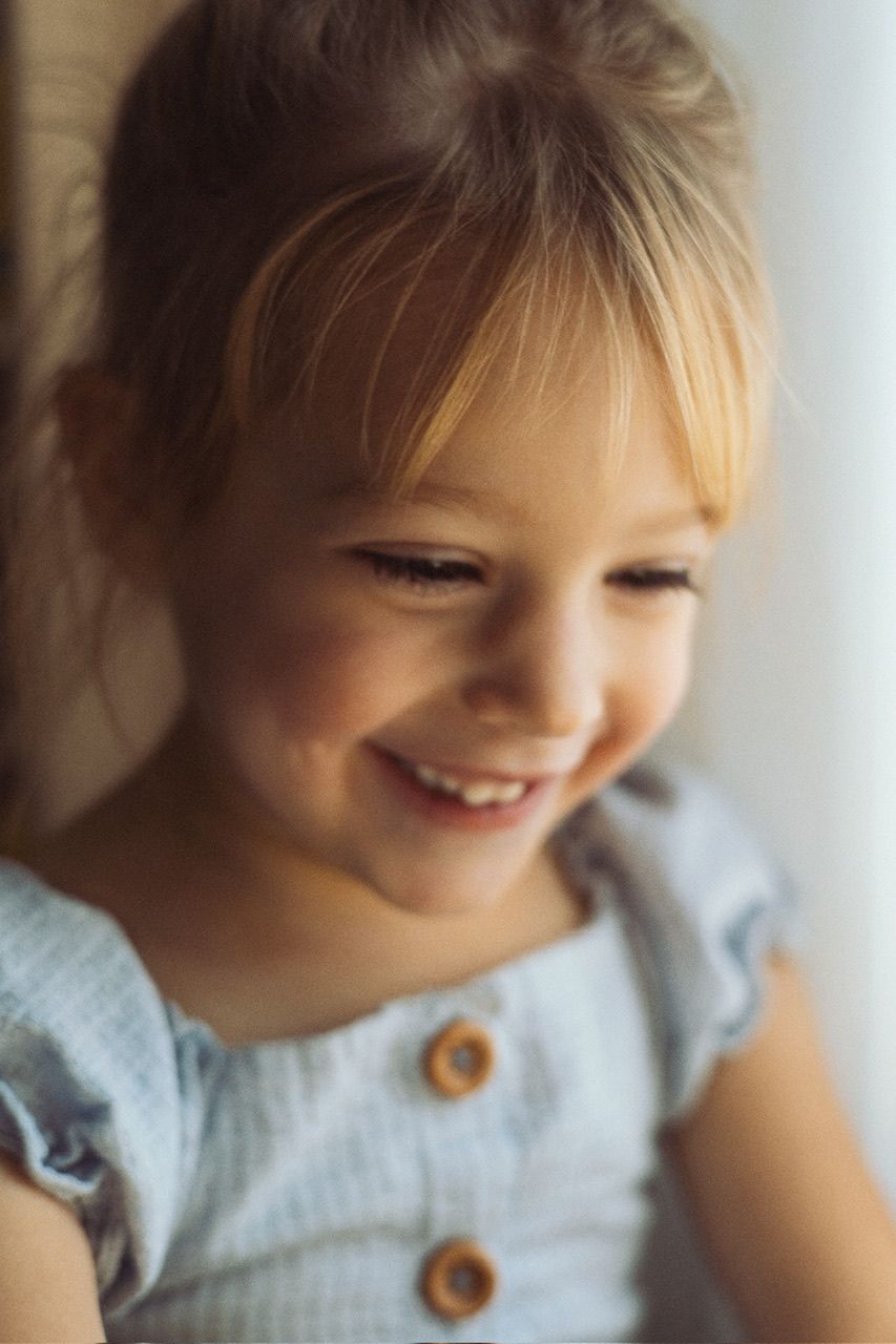 Child with bangs smiling sweetly in natural window light.