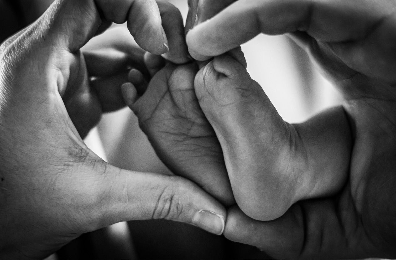 Black and white detail shot of hands tenderly touching in dramatic lighting.