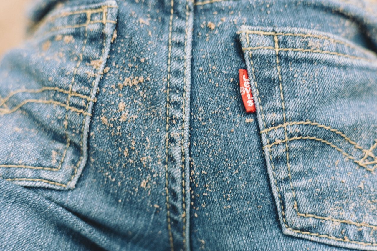 Close-up detail of worn denim jeans with speckled dirt pattern.