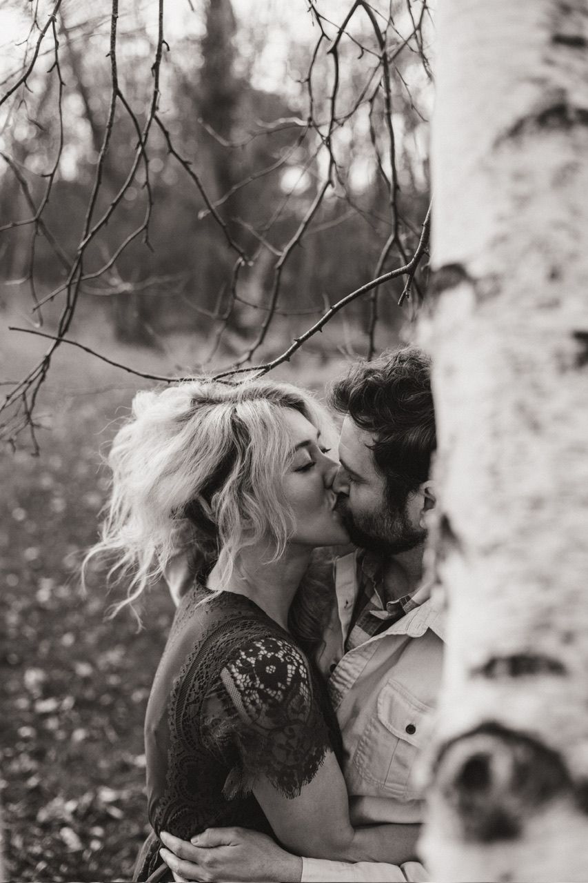 An intimate black and white portrait of a couple sharing a tender moment by a birch tree.