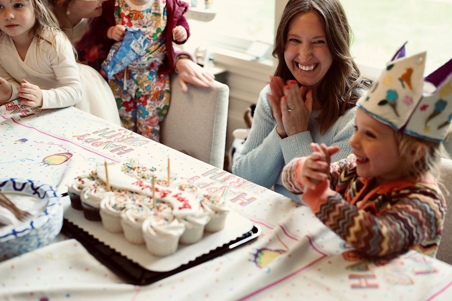 Birthday celebration with decorated cupcakes and paper crowns at a party table.