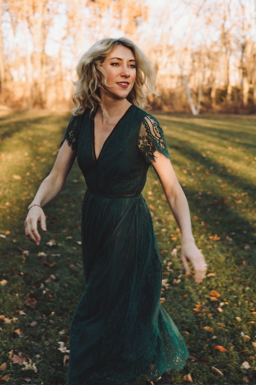 Woman in emerald green dress twirls gracefully in an autumn field at sunset.