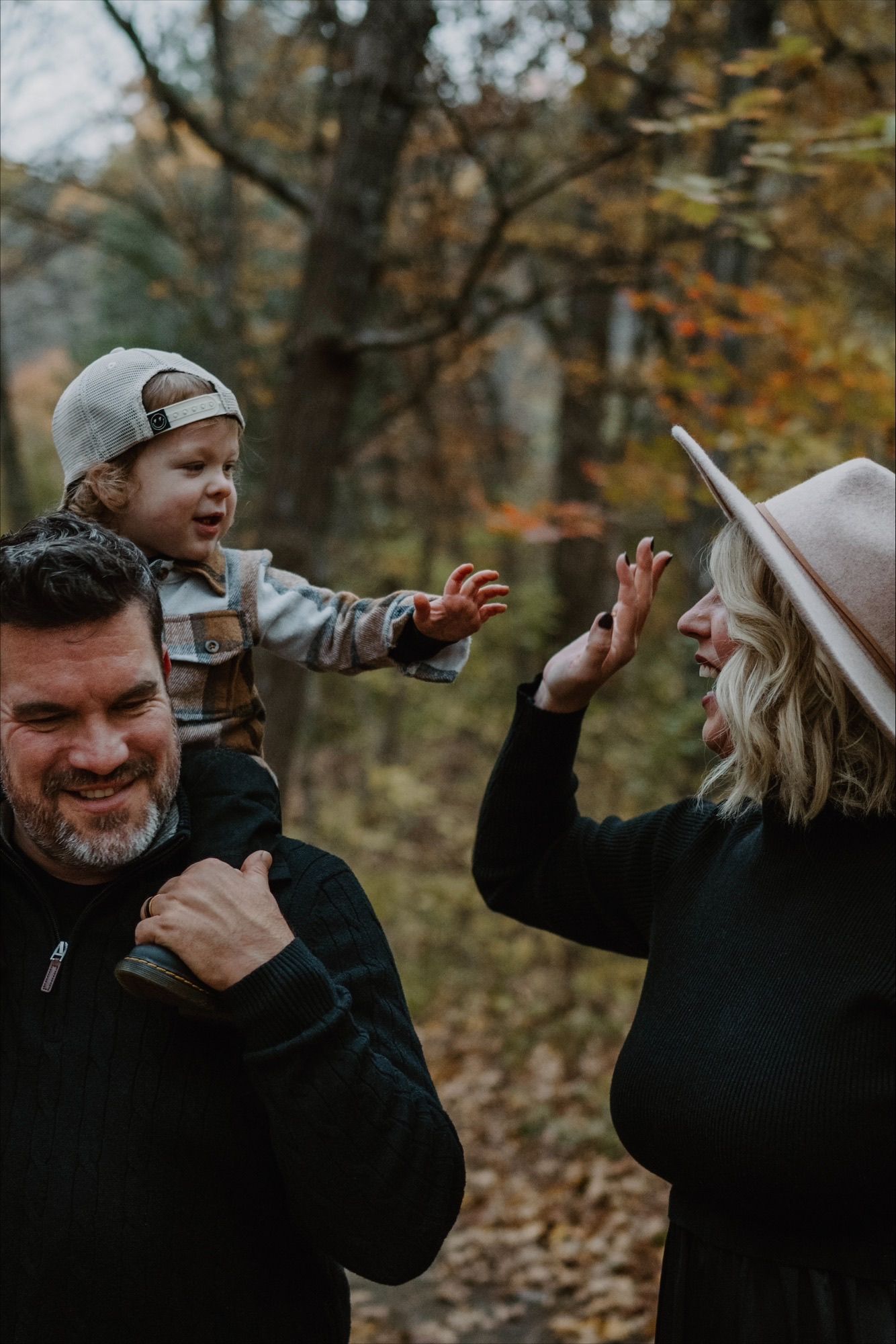 Playful autumn family photoshoot with casual outfits in a wooded setting.