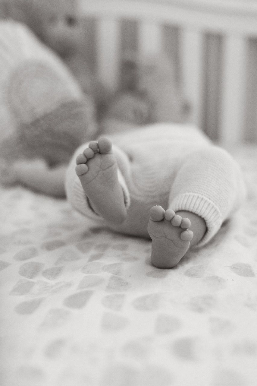 Black and white image of tiny newborn feet against patterned bedding.