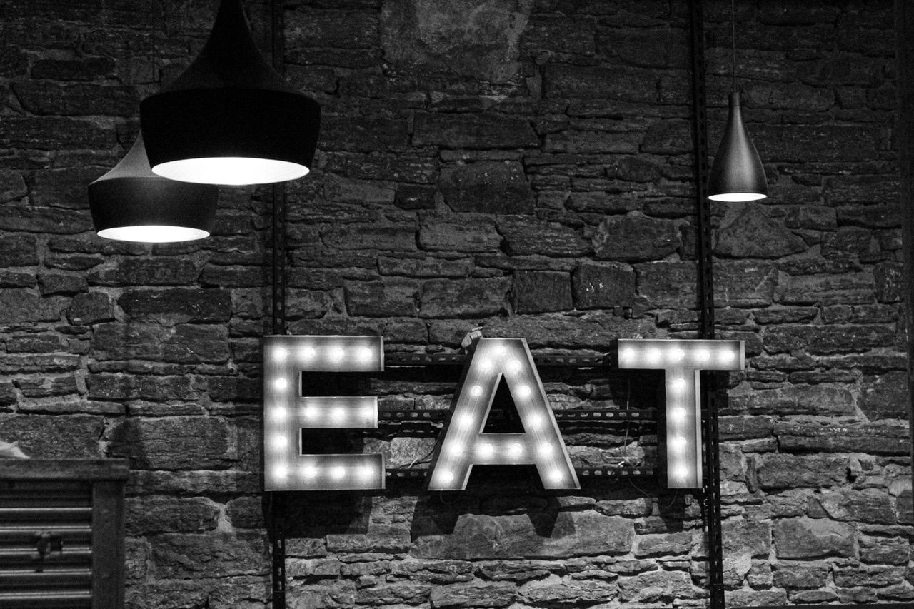 Dark brick wall with illuminated EAT sign letters mounted.
