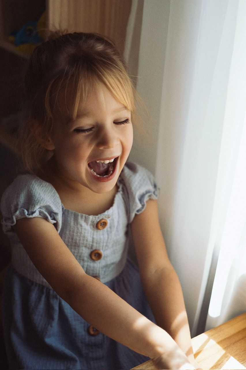 Young child playing and laughing while wearing a blue and white dress.