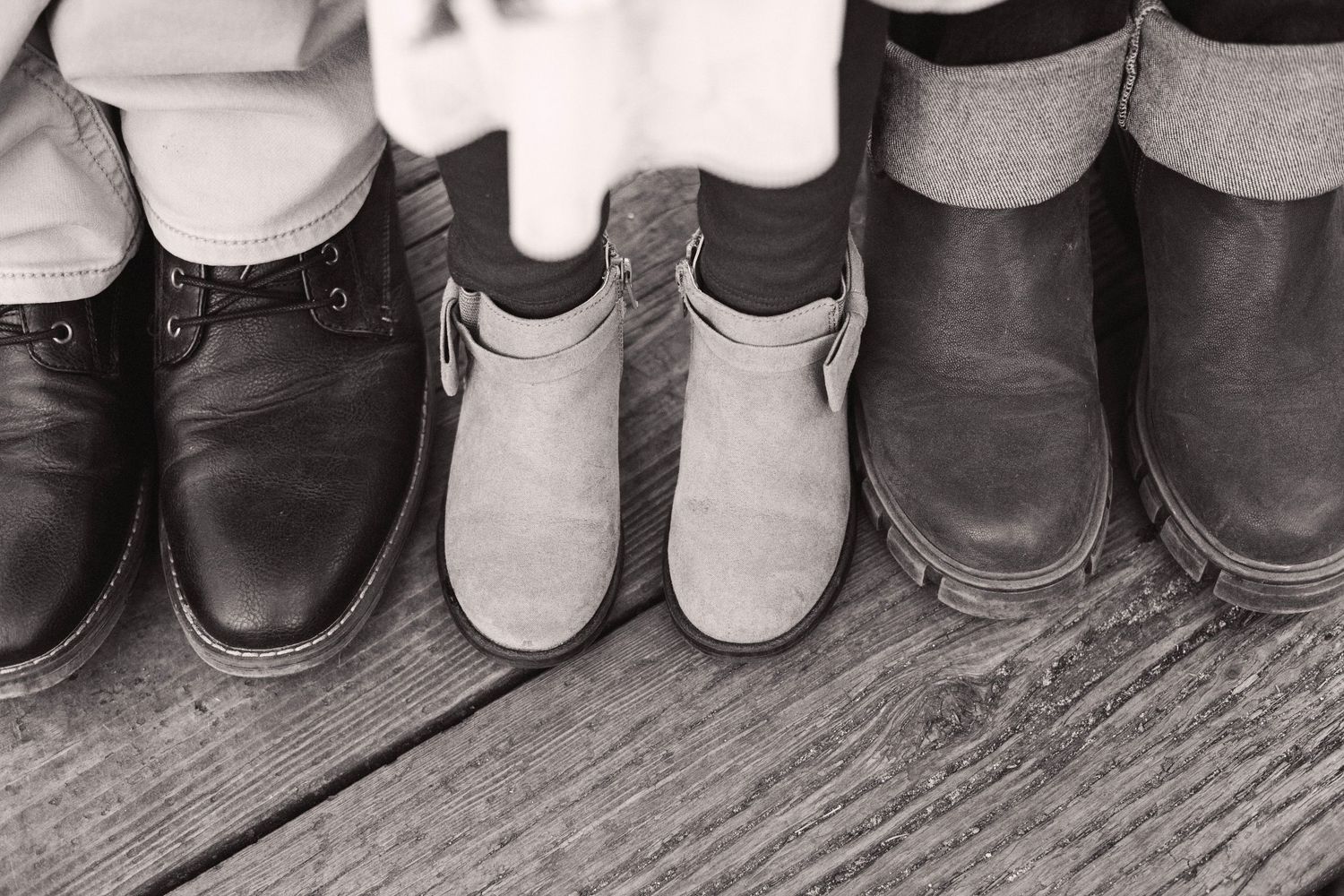 Black and white photo of three pairs of shoes lined up on rustic wooden boards.
