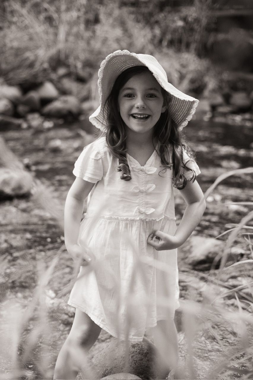 A joyful moment captured in black and white showing a child in a white dress and floppy hat outdoors.