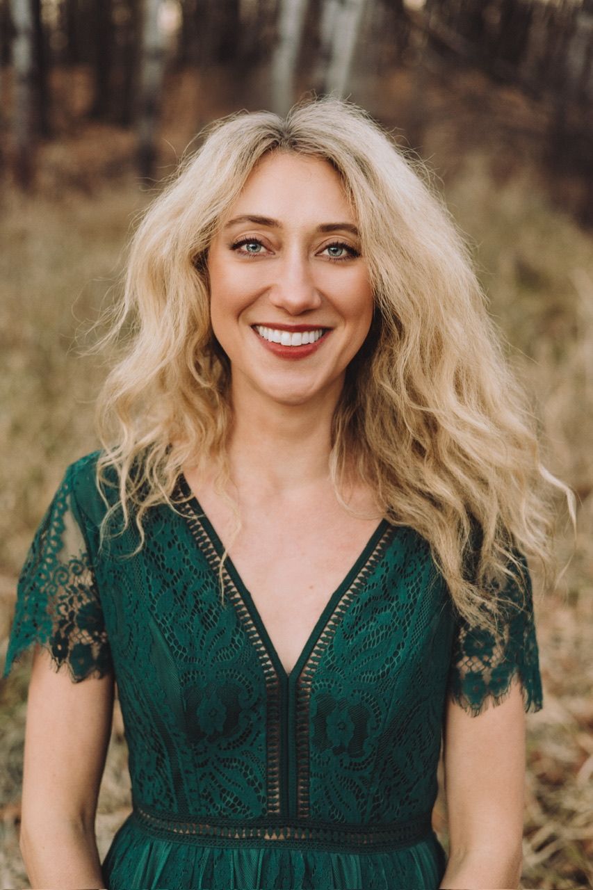 A woman in an emerald green lace dress poses outdoors in autumn.