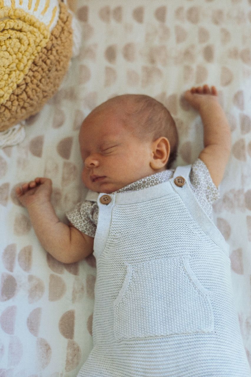 A sleeping newborn wearing white knit clothing on heart-patterned bedding.