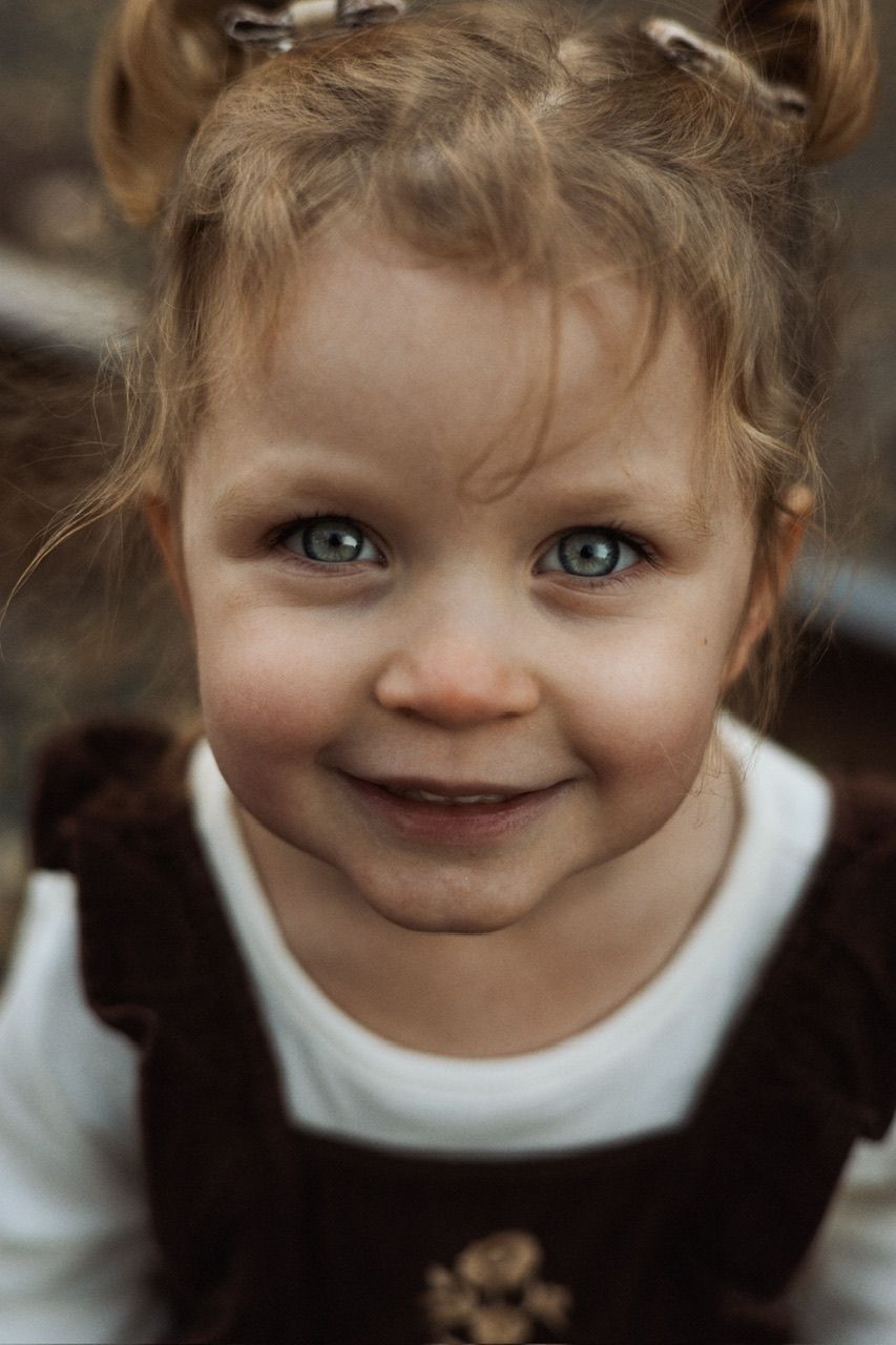 Close-up portrait showing bright blue eyes and a sweet smile wearing a white collar against dark clothing.