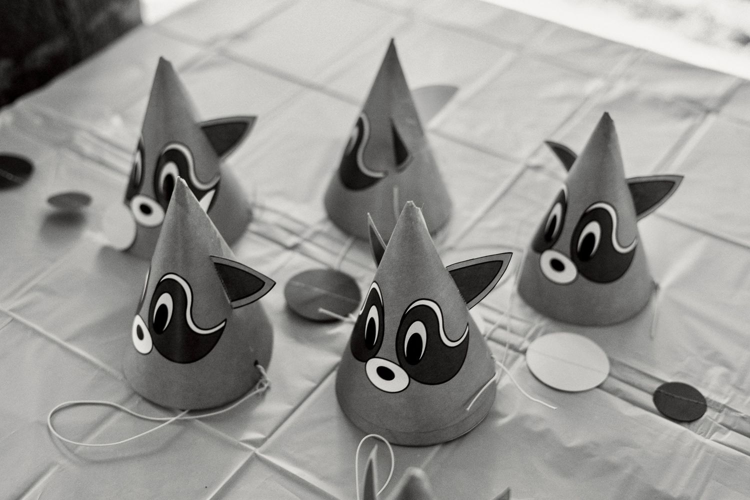 Black and white photo of gray party hats with decorative faces arranged on a table.
