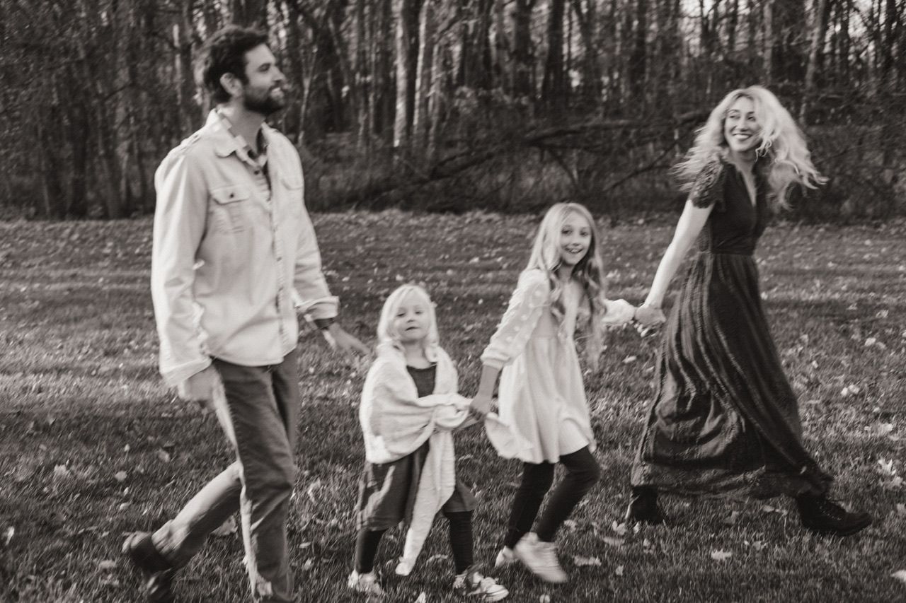 Black and white family portraits showing natural interactions outdoors among trees and fallen leaves.