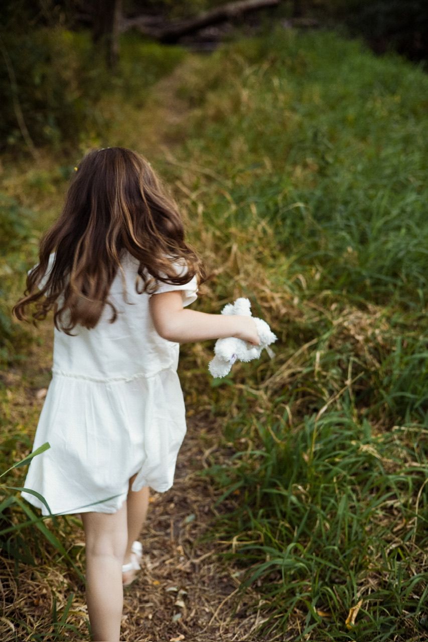 Child in white dress running along a nature trail while holding something in their hand.