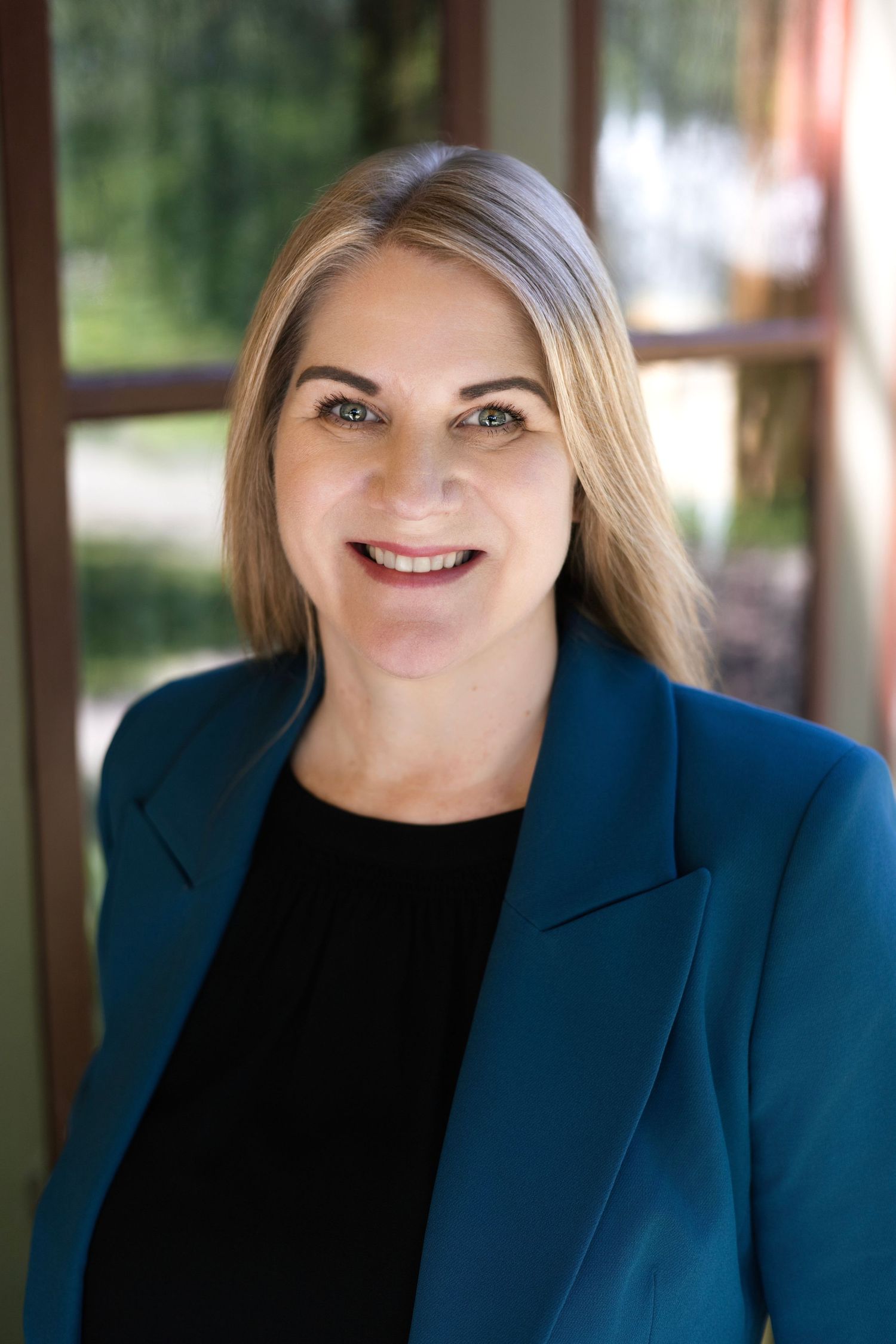 Professional portrait of a woman in blue blazer and black top against a blurred background.
