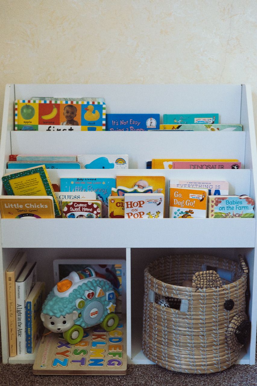 White wall-mounted bookshelves filled with colorful children's books and woven storage baskets.