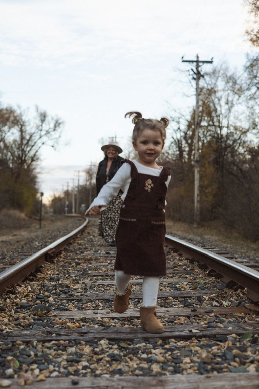 Small child in overalls playing on train tracks covered in autumn leaves.