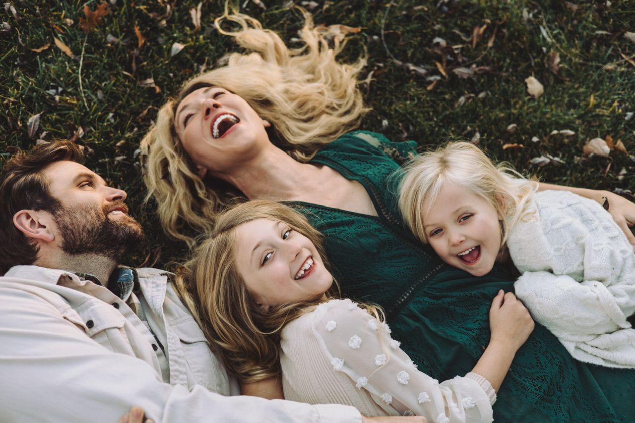 Family lying on autumn ground sharing joyful laughter together.