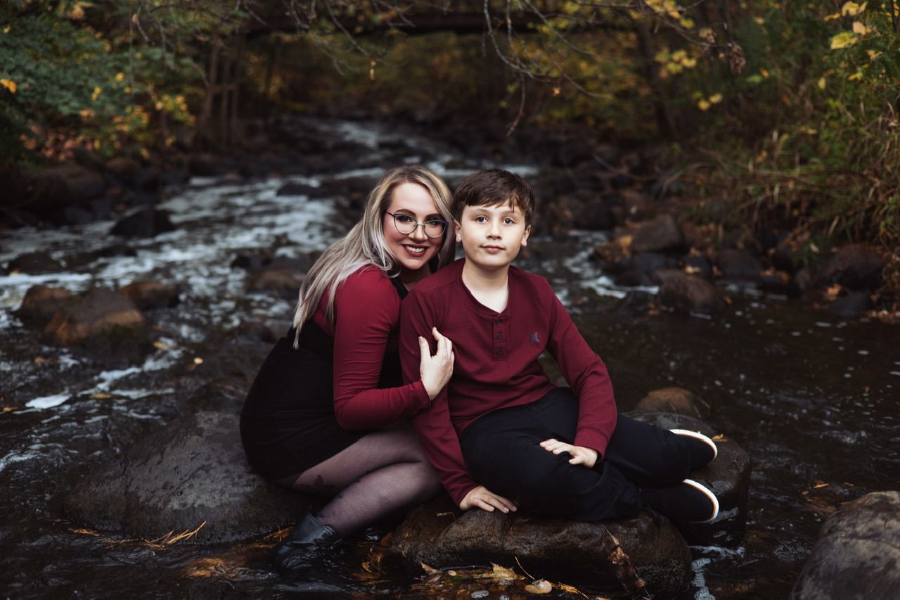 Family photo session by a scenic stream in autumn with burgundy clothing.