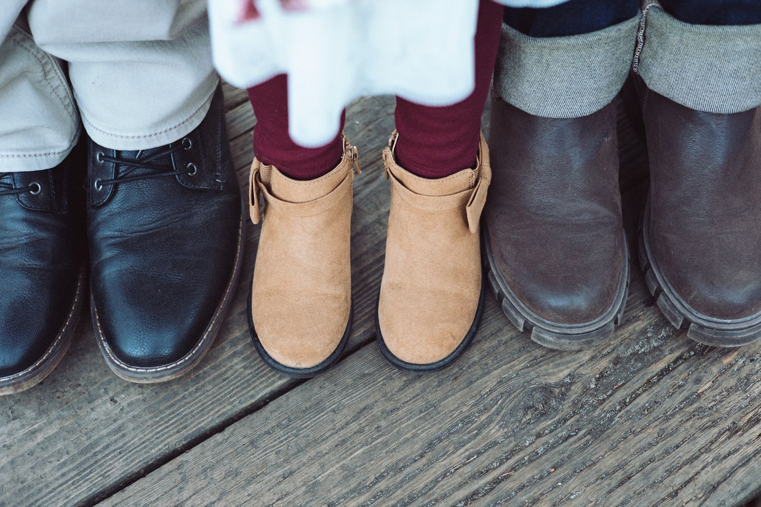 Three pairs of shoes lined up on a wooden deck showing black leather, tan suede, and brown leather footwear.