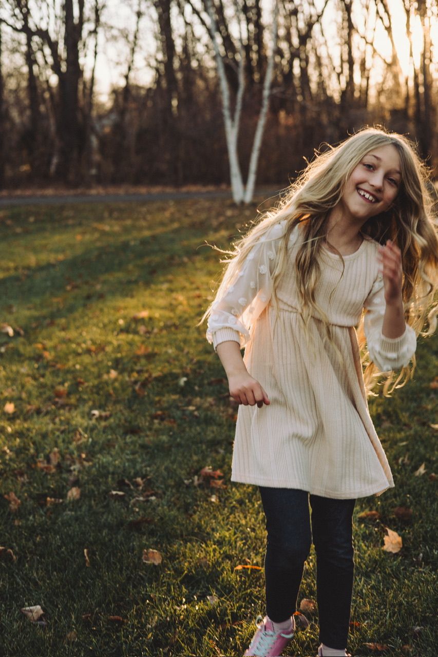 Dancing and twirling in a cream sweater against an autumn sunset with trees in the background.