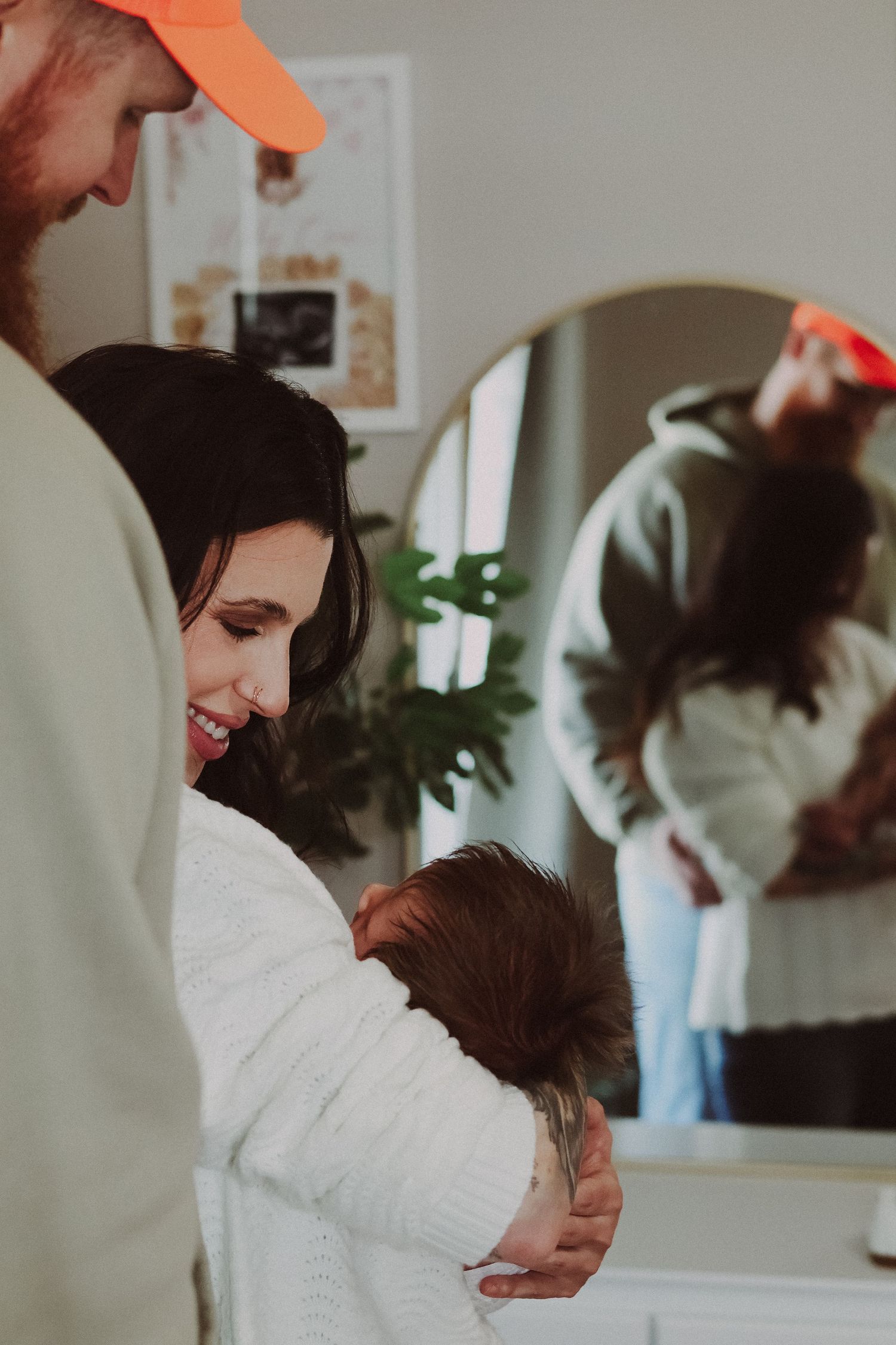 Intimate family moment captured as parents embrace their baby in warm indoor lighting.