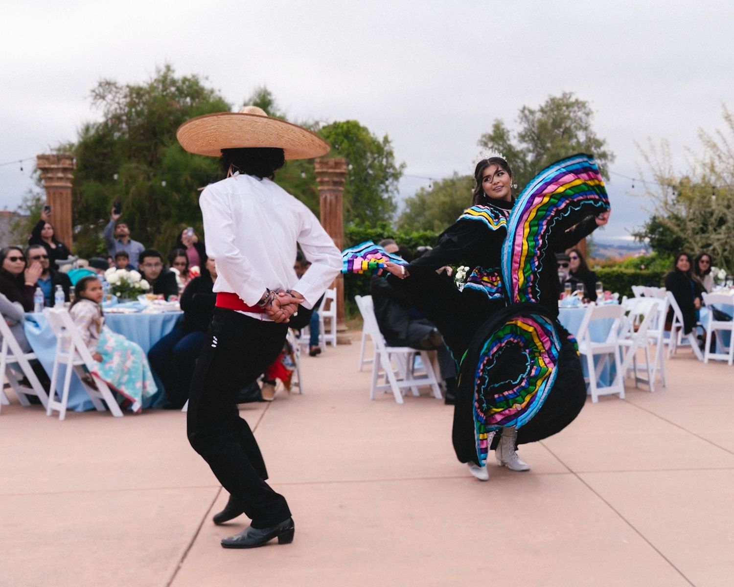 Traditional Mexican folkloric dancers performing Jarabe Tapatio in colorful costumes at an outdoor wedding reception.