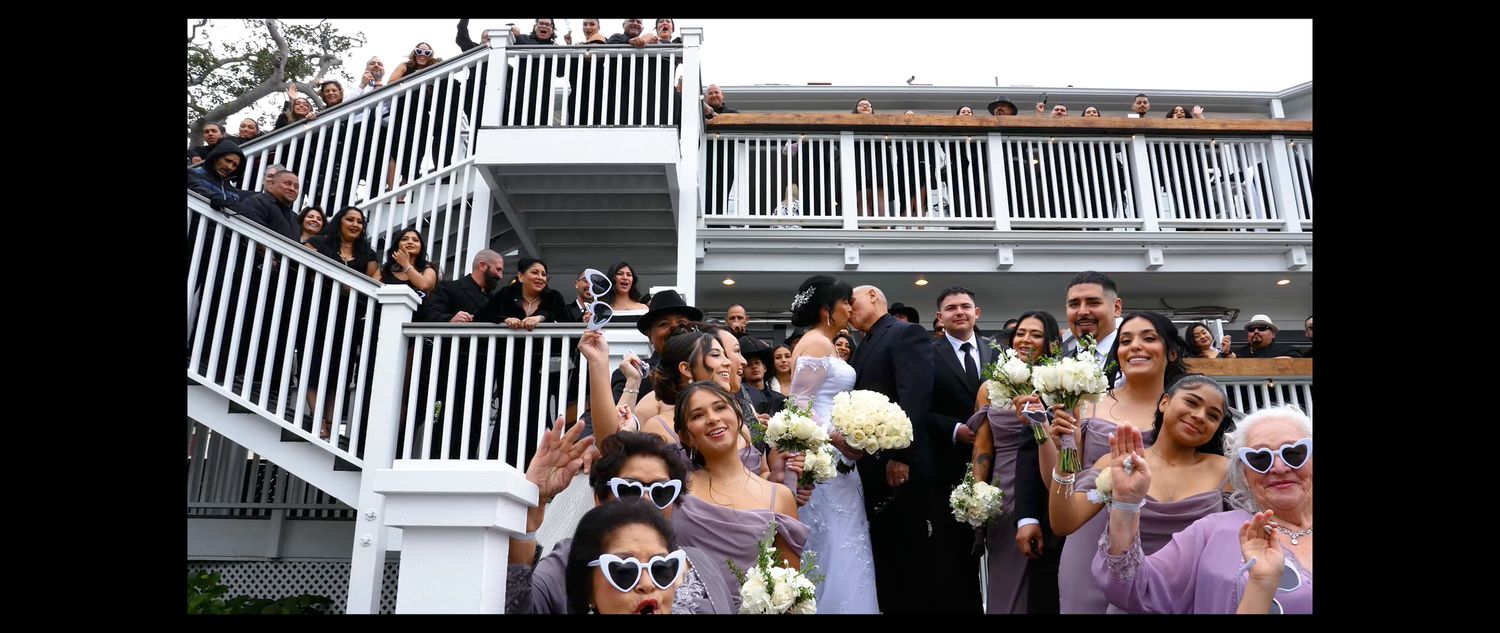 Large wedding party poses on white staircase steps outside elegant venue with bridesmaids in lavender dresses.