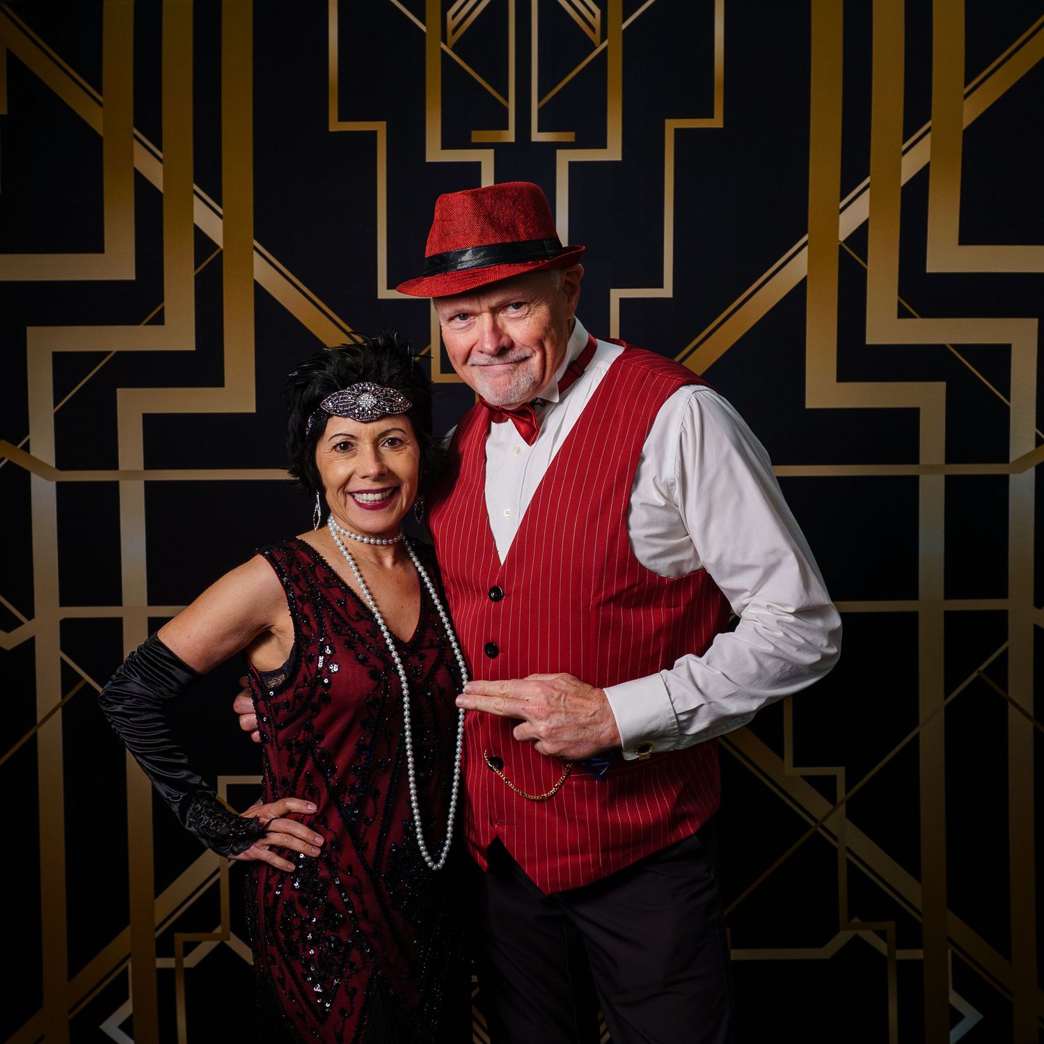 Couple in 1920s Great Gatsby costumes posing in front of Art Deco backdrop at themed party.