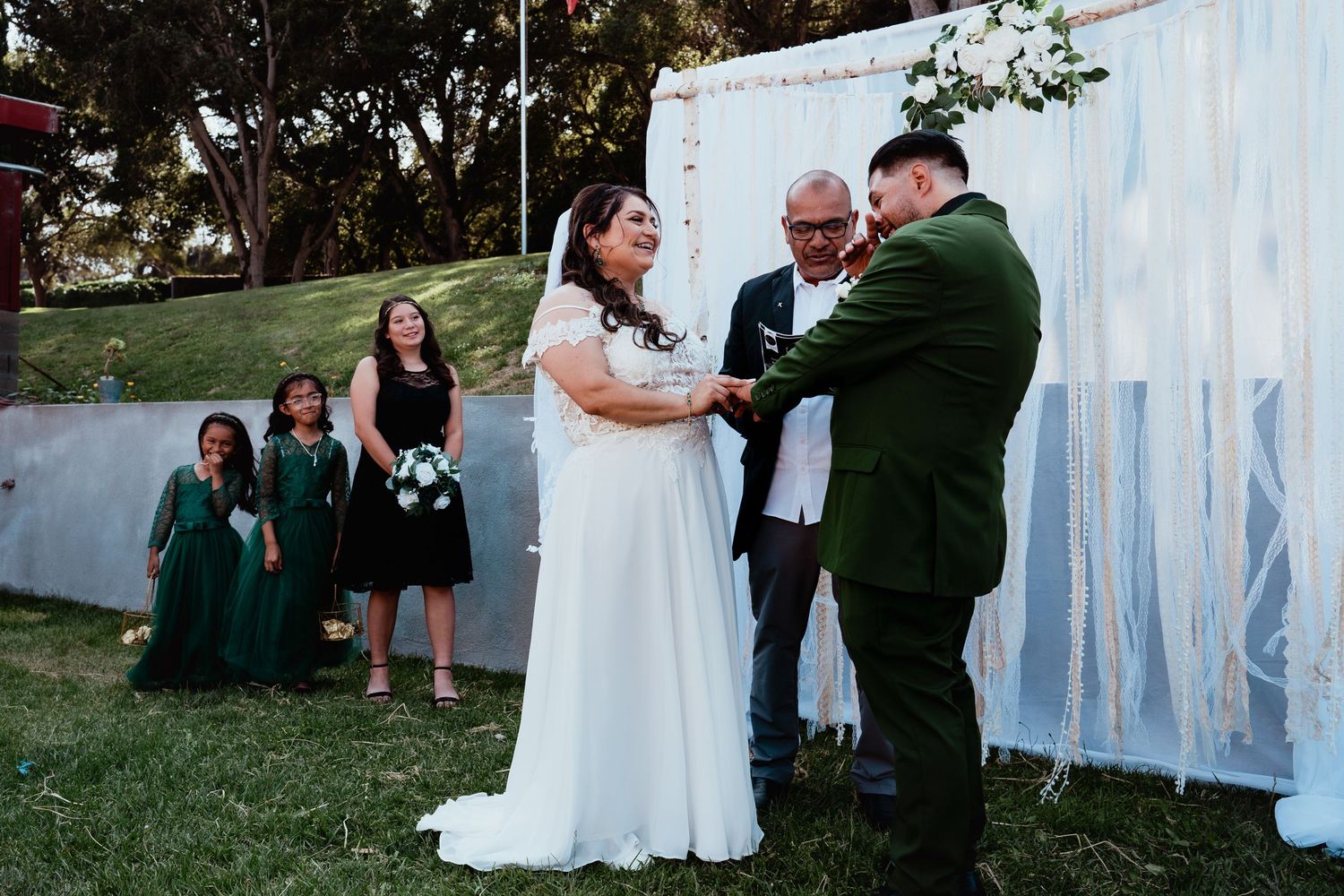 A couple shares their first dance at an outdoor wedding reception with blue drapery and guests watching in the background.