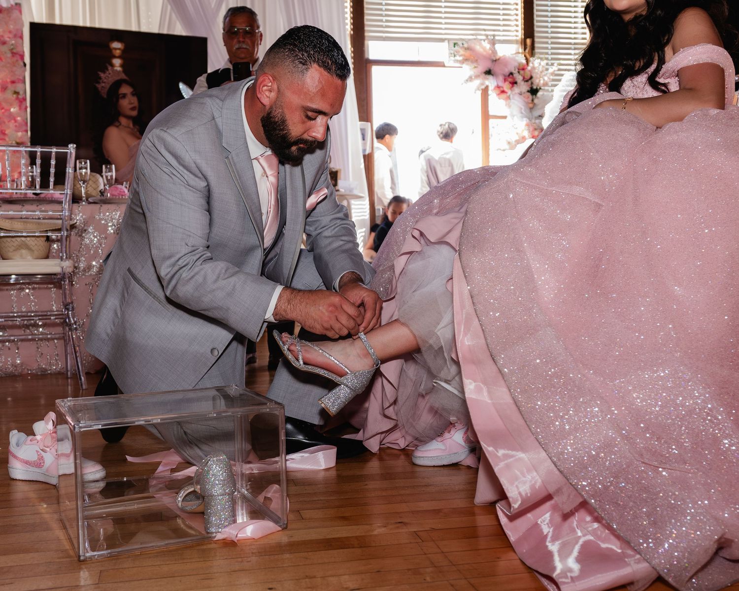 Man in gray suit placing a heel on a woman in a pink ball gown during a quinceañera ceremony.