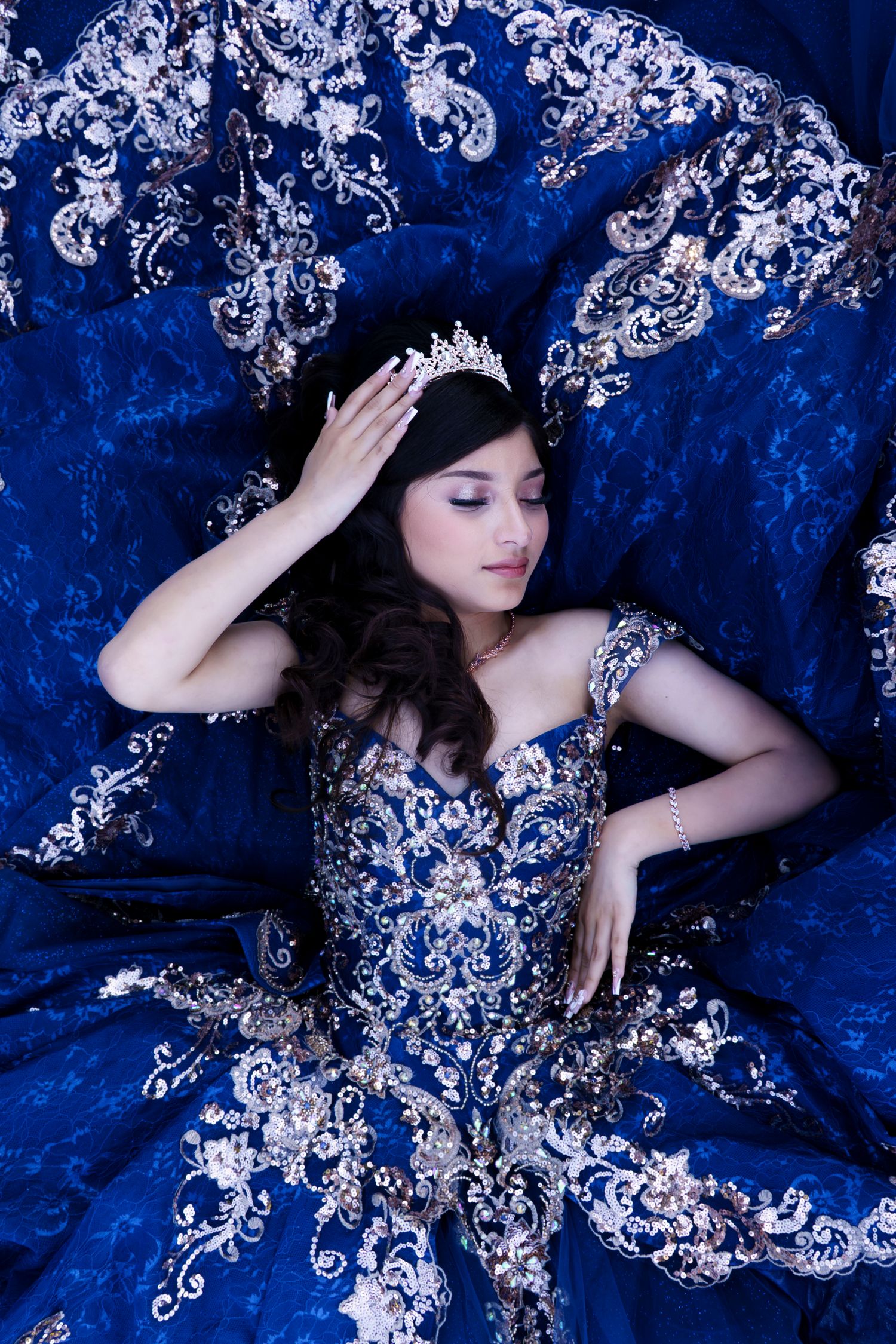 Ornate royal blue ball gown with silver embellishments displayed against deep blue velvet backdrop.