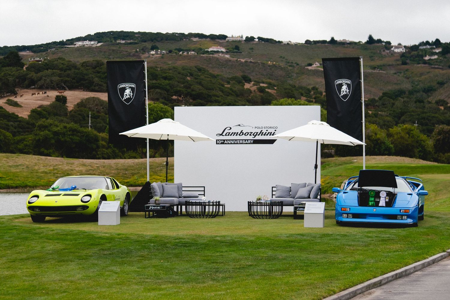Two classic Lamborghini cars displayed at an outdoor Lamborghini branded event with white backdrop and patio seating.