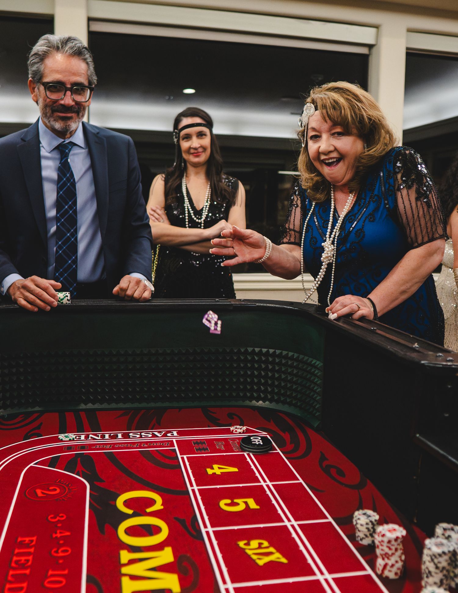 Guests in 1920s attire laugh and celebrate at a craps table during a glamorous casino-themed party event.