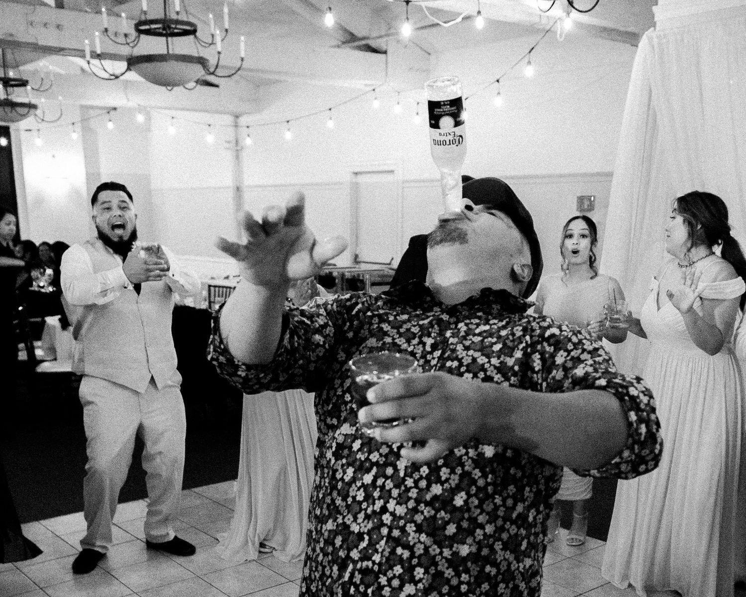 A black and white photograph of a lively indoor celebration with people dancing and laughing in a decorated room.