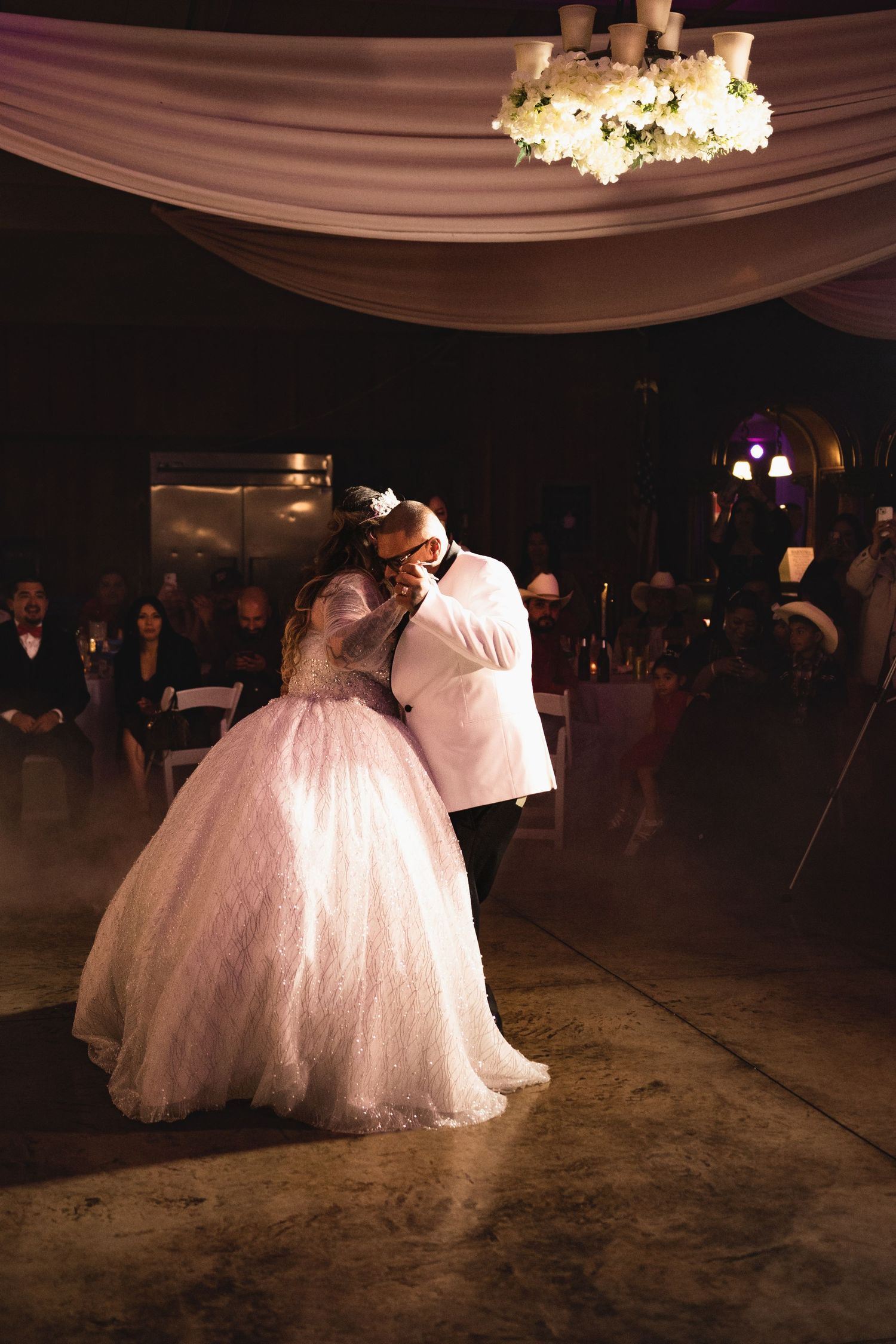 Romantic first dance at a wedding reception under draped fabric ceiling and chandeliers.