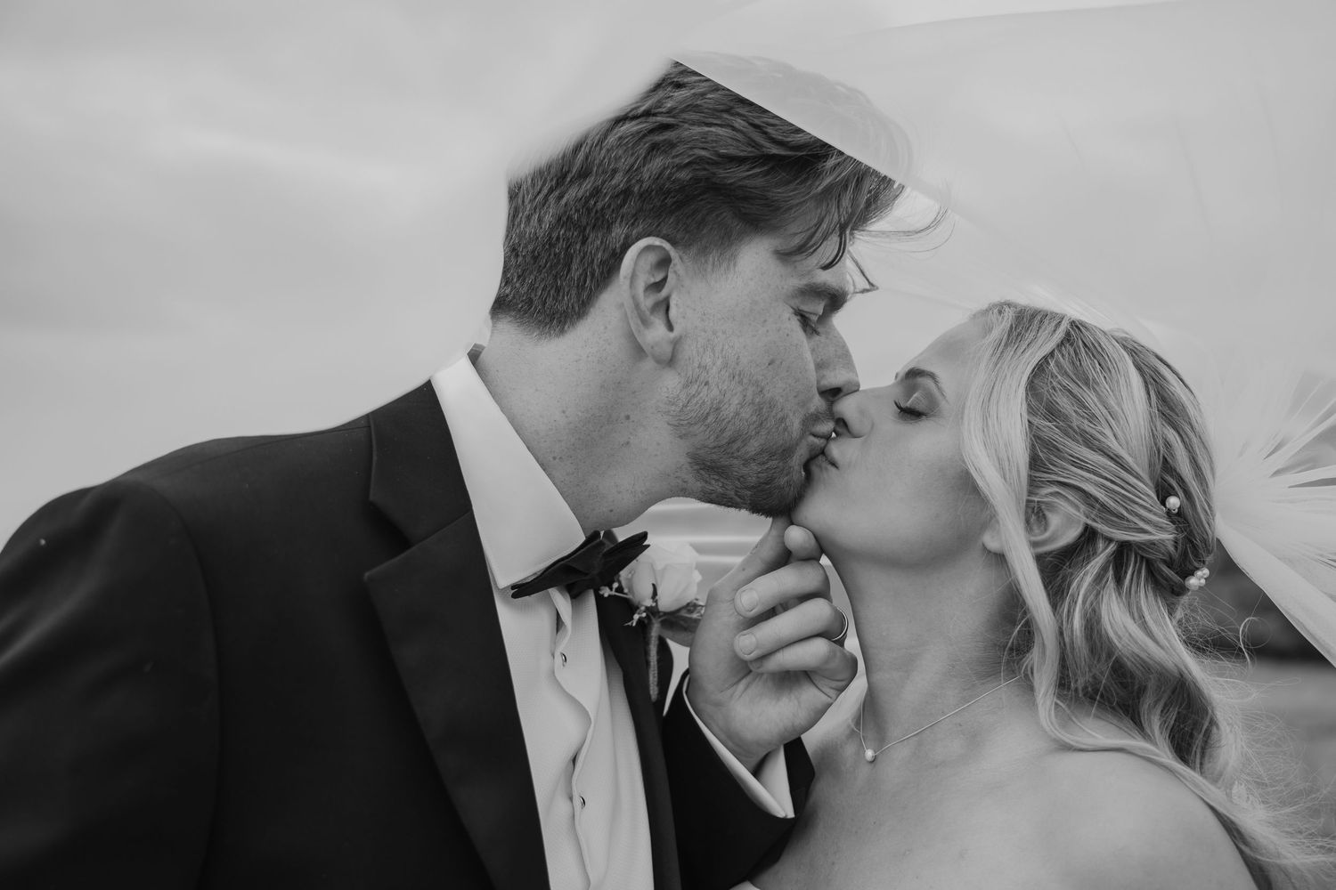 Black and white photo of a bride and groom sharing a romantic kiss on their wedding day.