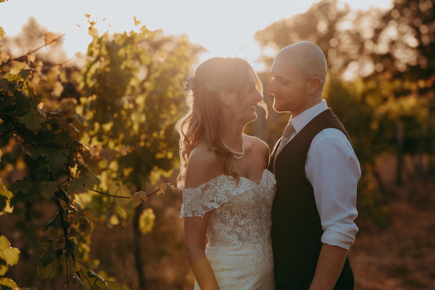 Bride and groom share a romantic moment in a sun-drenched vineyard, with golden light illuminating their wedding attire.