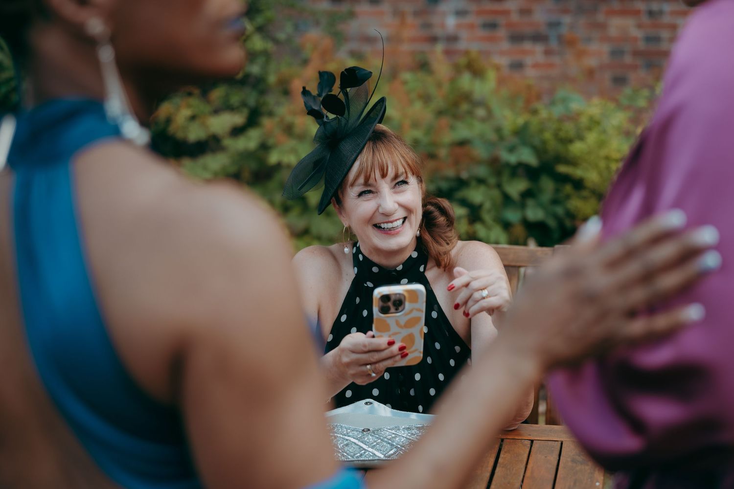 Woman in polka dot dress and black fascinator hat smiling at a garden party event.