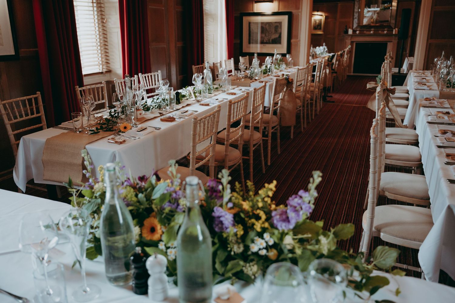 Elegant wedding reception room with long tables, floral centerpieces, and Chiavari chairs in a warm, wood-paneled venue.