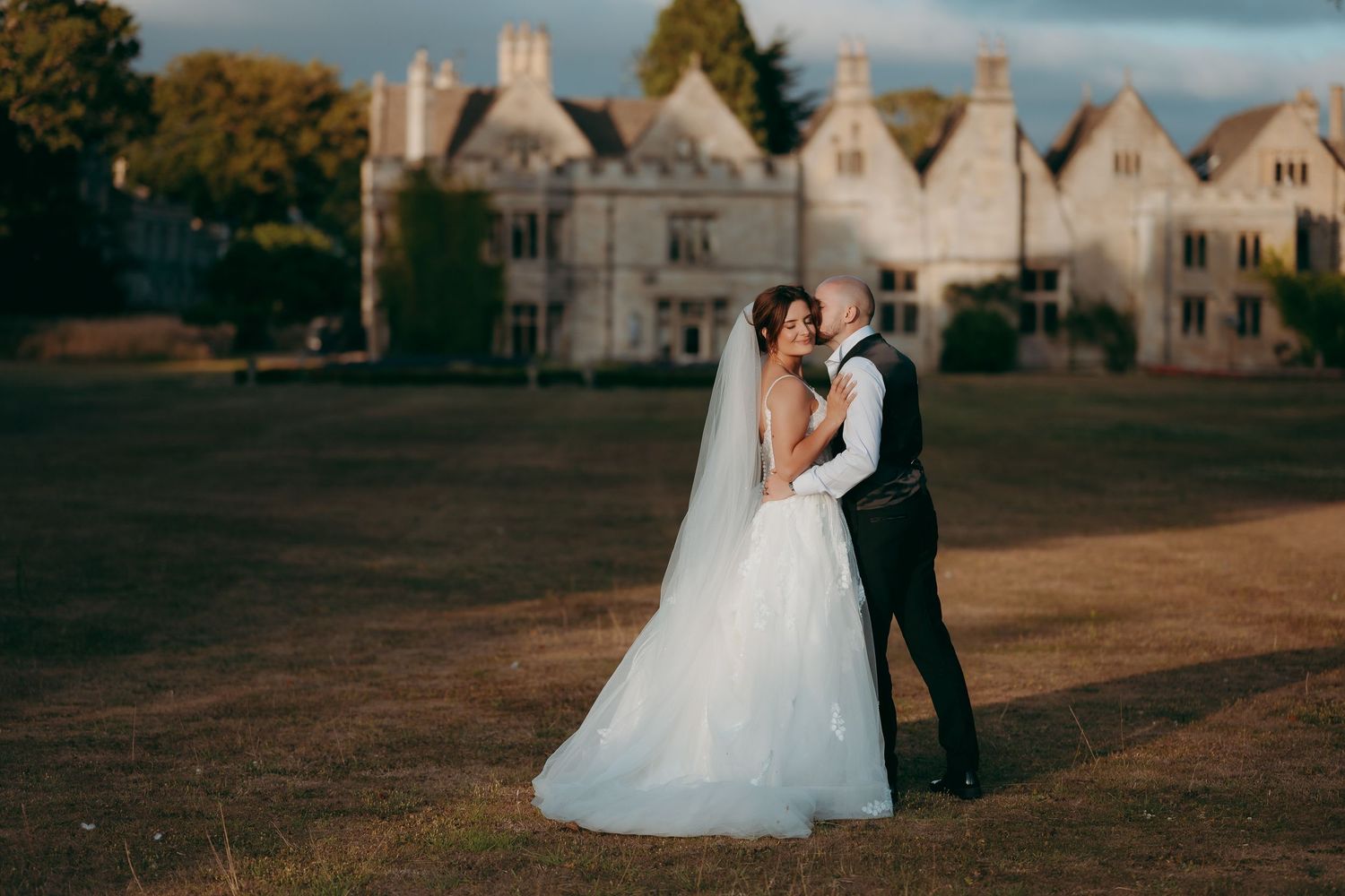 Bride and groom embracing on a lawn in front of a grand manor house at golden hour.