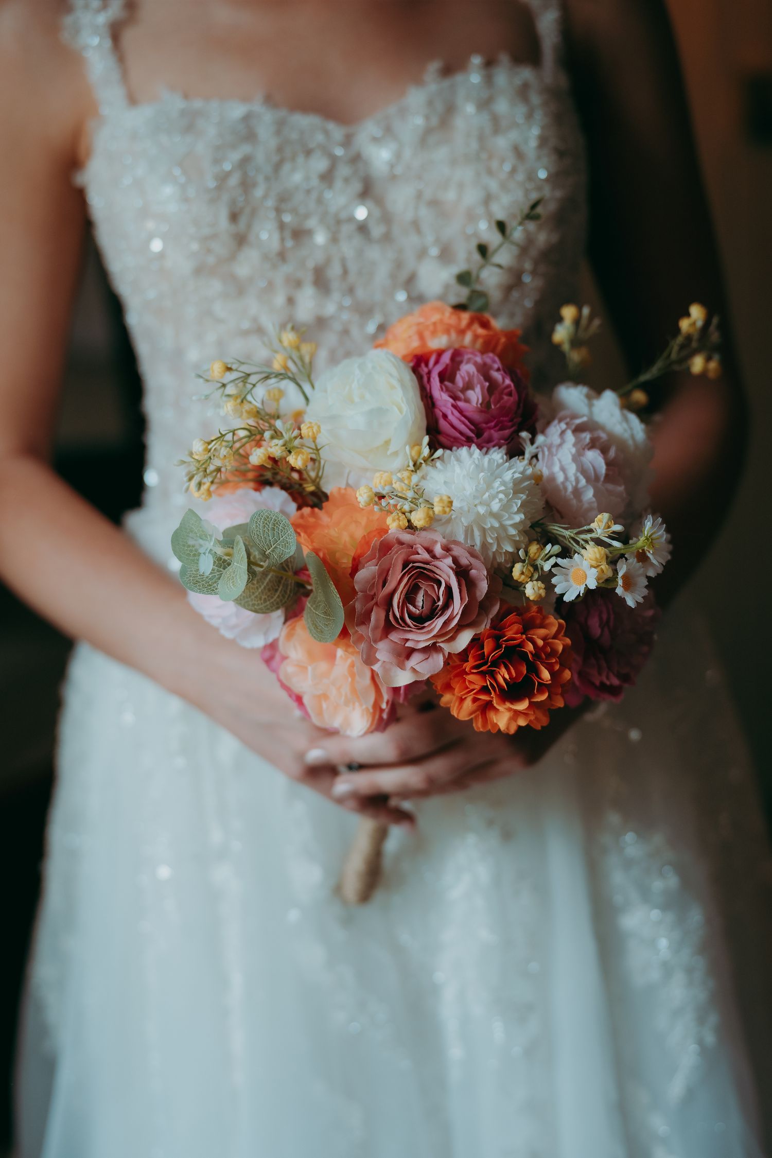 Bride in white sequin gown holding colorful wedding bouquet with roses, dahlias, and wildflowers in pink, orange, and cream.